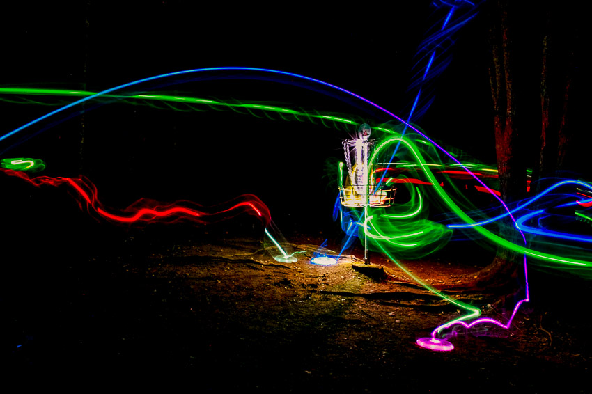 Glow in the dark disc golf disc lights shining on a basket